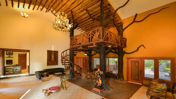 A spacious lobby with a central tree structure, a staircase, and a chandelier. - Syna Tiger Resort - Bandhavgarh (Manpur)