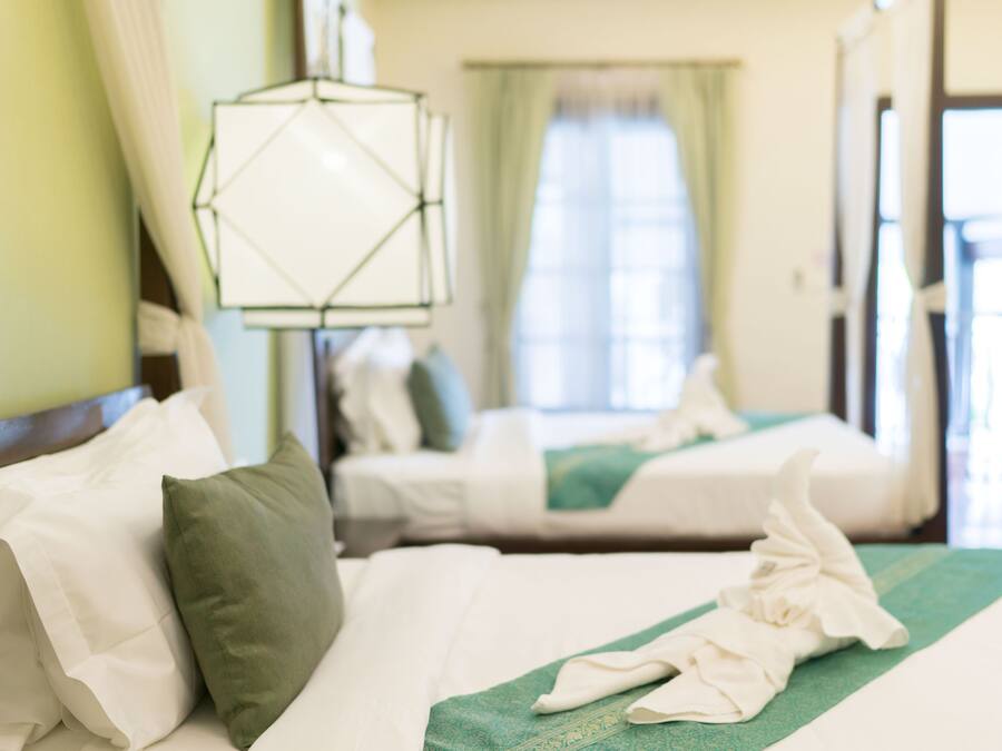 A hotel room with two beds, each with white linens and a green accent.