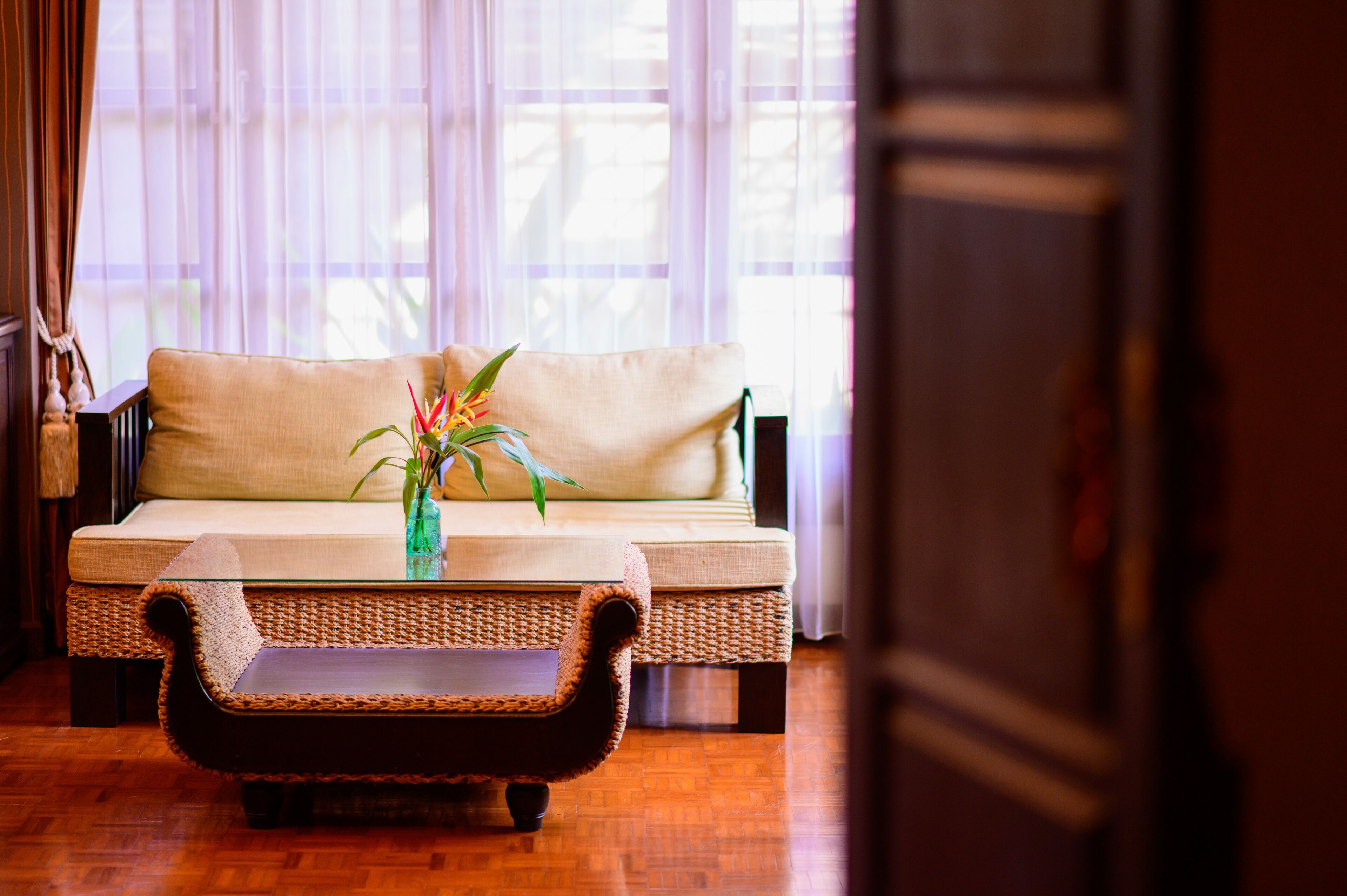A wicker sofa with a cushion, a glass coffee table, and a vase with a plant.
