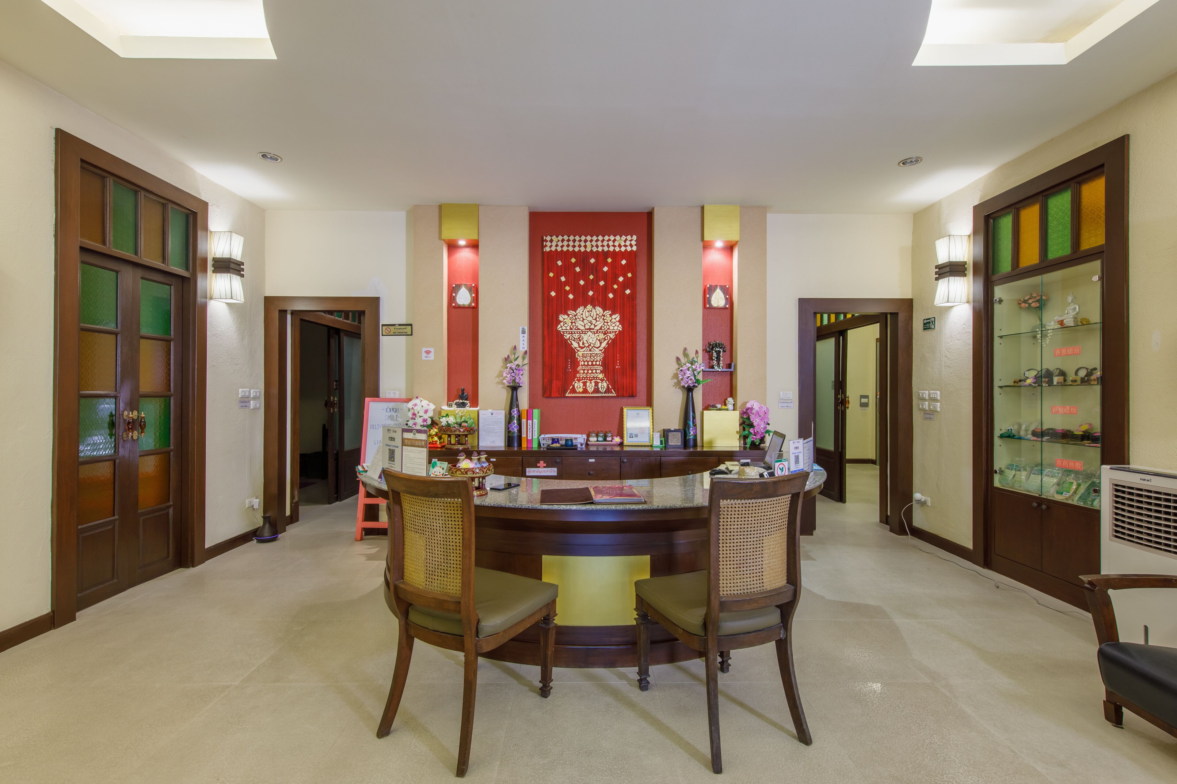 Un área de recepción con un mostrador central, dos sillas, un panel decorativo rojo y vitrinas de vidrio.