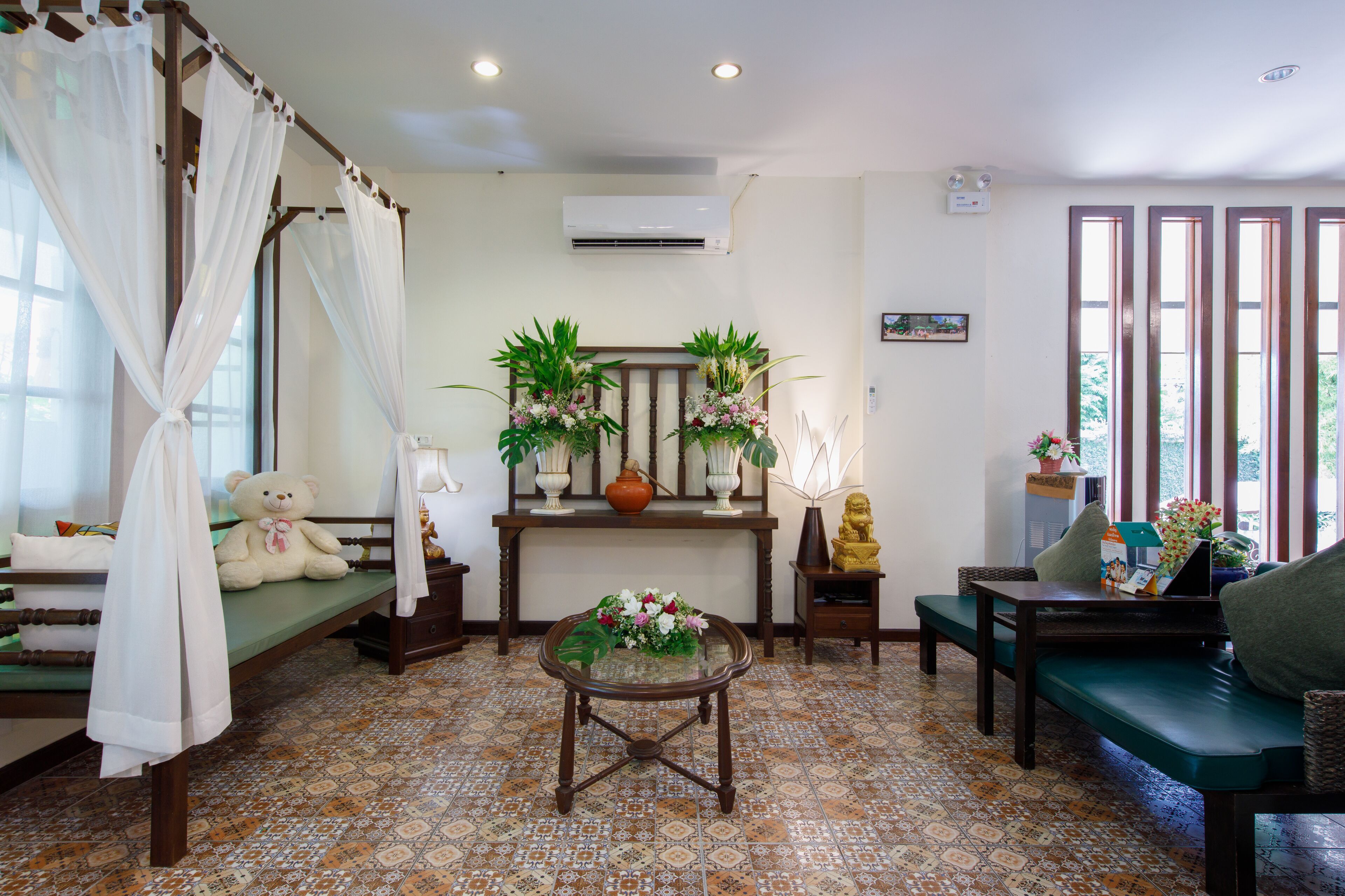 A room with a bed, a sofa, a table with a vase of flowers, a teddy bear, and a statue.