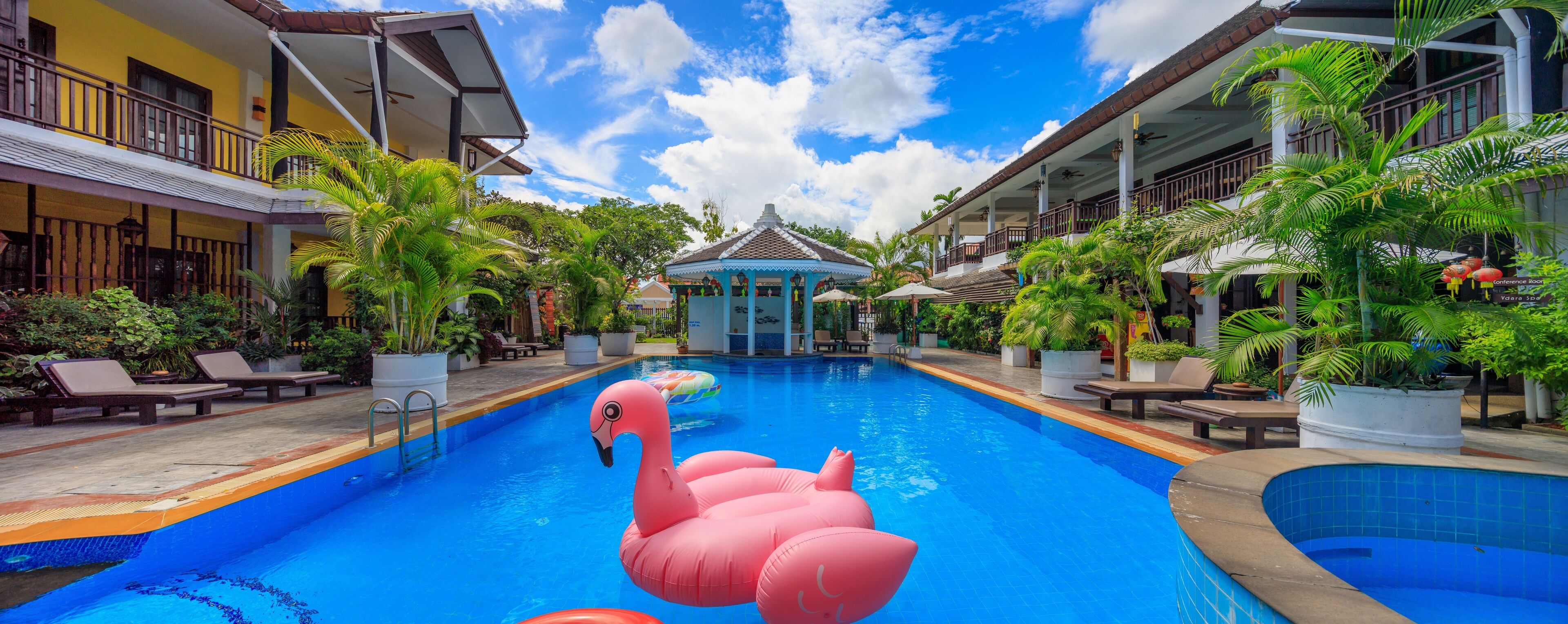 A pool area with lounge chairs, a decorative flamingo float, and a gazebo in the center.