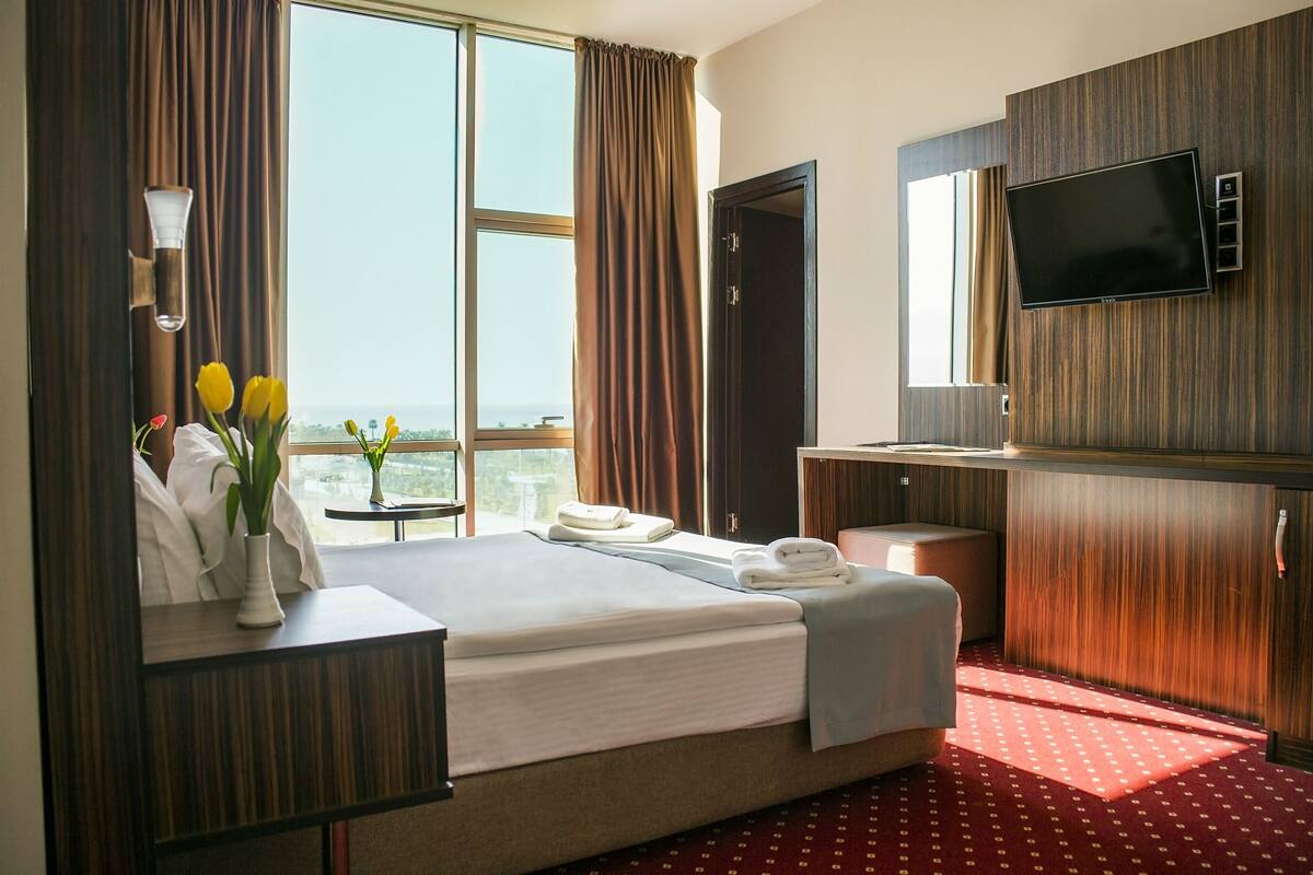 A hotel room with a large bed, a desk, a TV, and a view of the city.