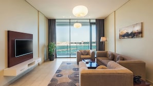 Un salon moderne doté d’un téléviseur à écran plat, de sièges confortables, d’une grande fenêtre donnant sur une marina et d’un tableau accroché au mur.