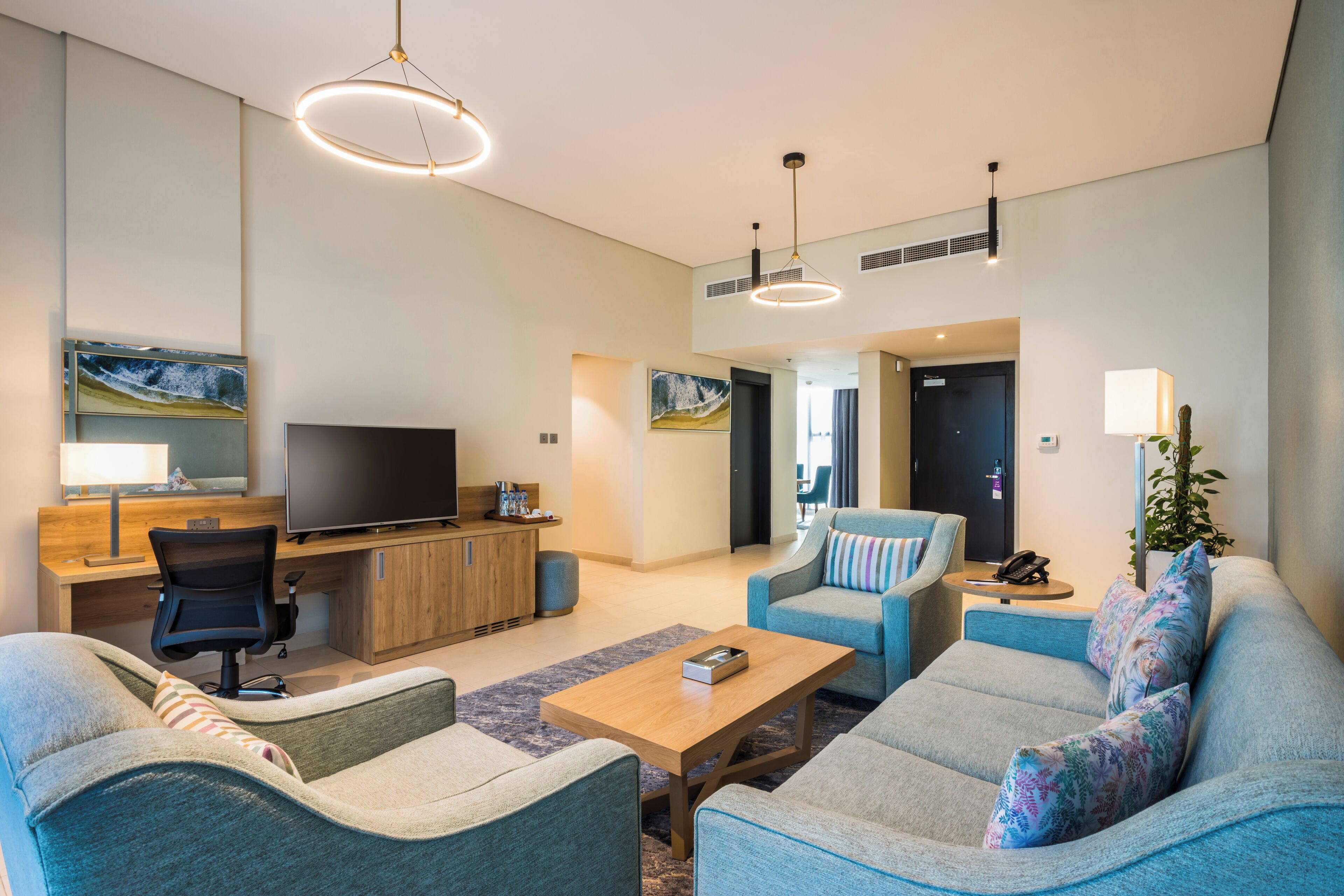 A modern living room with a flat-screen TV, a wooden desk, and a blue sofa.