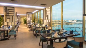 Un espace de restauration moderne, avec des tables dressées pour le service, de grandes fenêtres offrant une vue sur la ville et un aménagement intérieur épuré et contemporain.