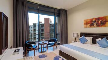 A hotel room with a large bed, a desk, two chairs, a small table, a lamp, and a painting on the wall.