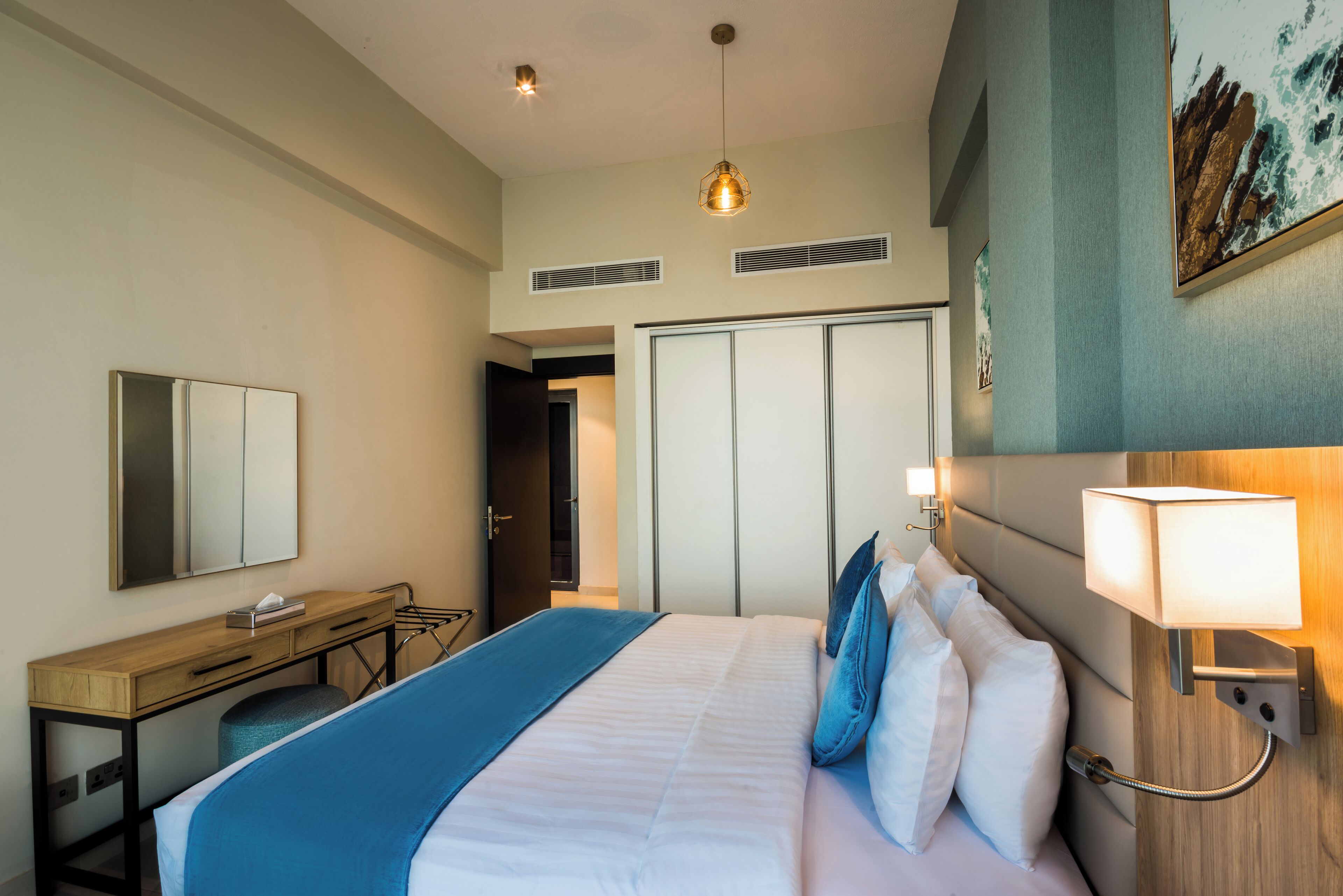 Ein Hotelzimmer mit Bett, Nachttisch und Schreibtisch. Eine Tür führt in einen weiteren Raum.