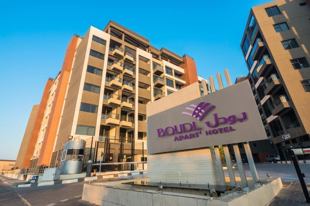 A hotel sign with the name "BOUDL APART HOTEL" and a modern building in the background.