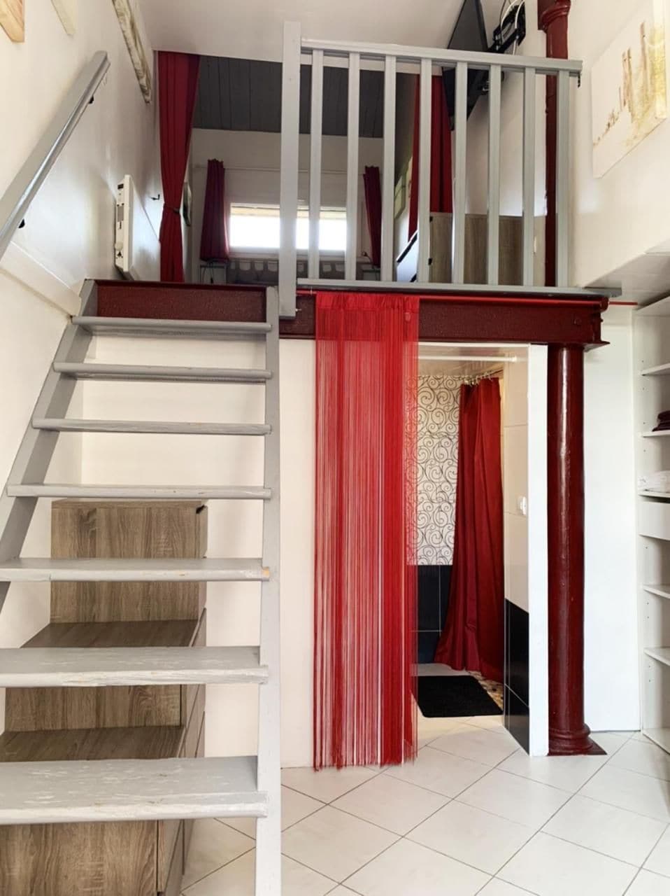 Eine Holztreppe führt zu einer Zwischenebene mit einem roten Vorhang.