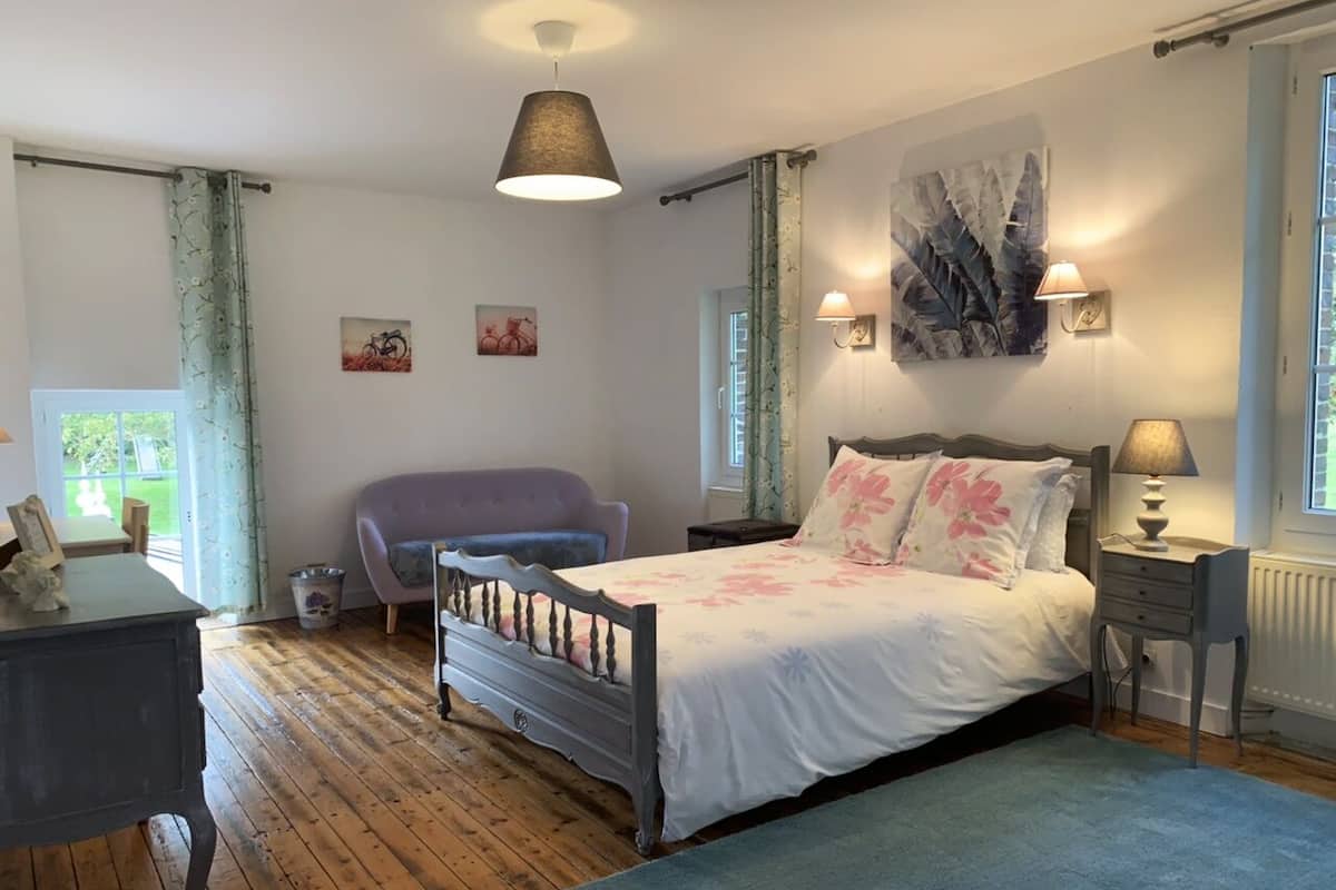 Un dormitorio con suelo de madera, una cama con ropa de cama estampada, una silla, un escritorio y una lámpara.
