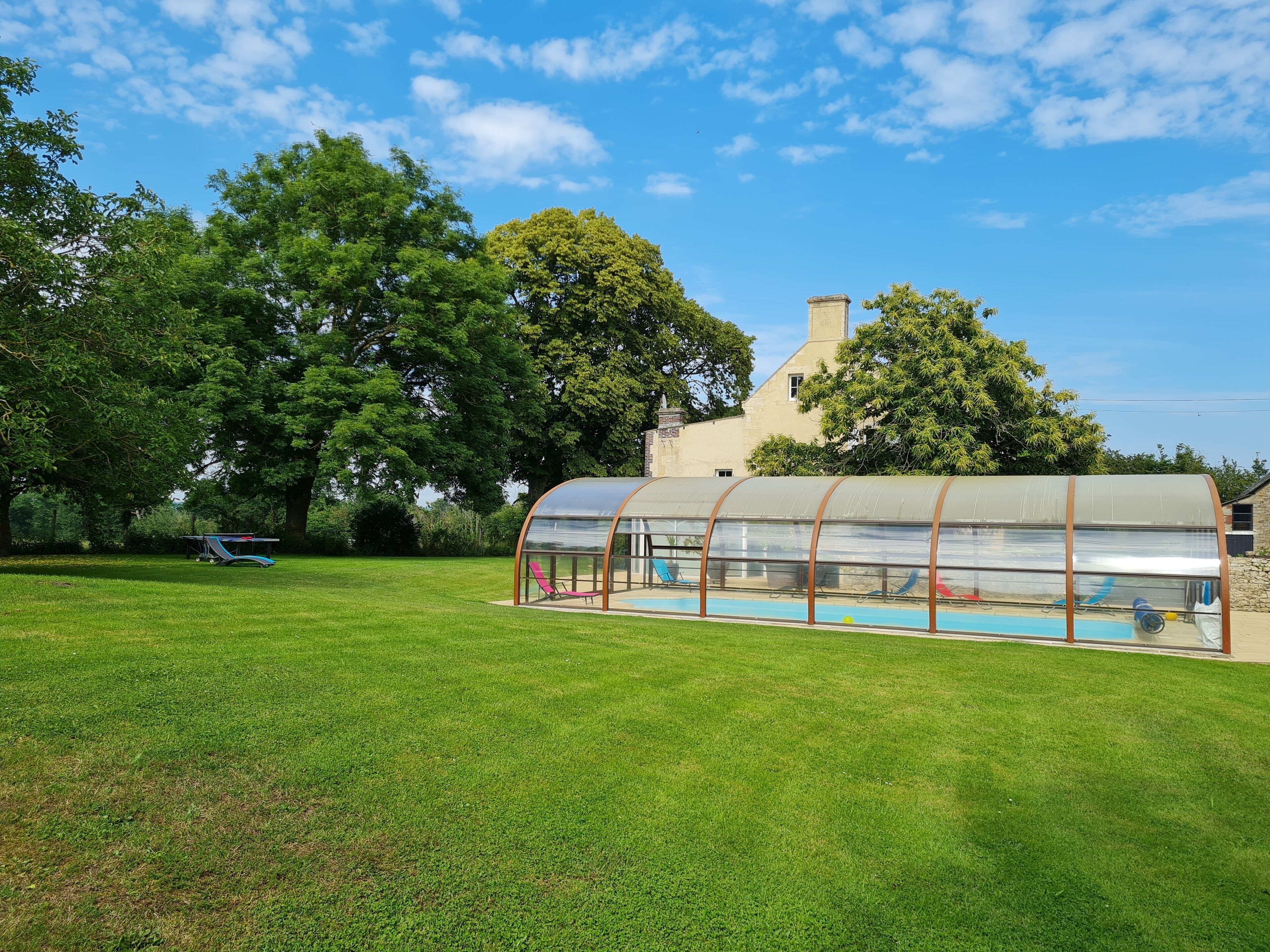 A large, covered swimming pool with a transparent roof, surrounded by a well-maintained lawn and trees.