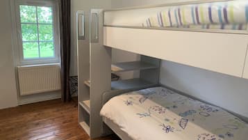 Una cama litera con colchón blanco y cabecero colorido. Se ve una ventana con vistas al exterior, con vegetación.