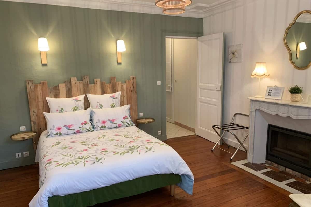 Un dormitorio con cabecera de madera, colcha estampada con motivos florales, chimenea y dos lámparas fijadas a la pared.