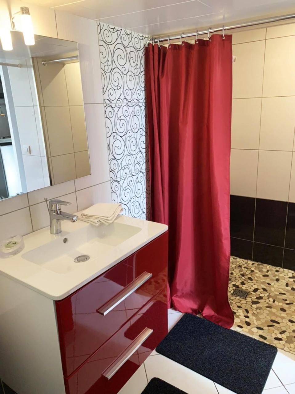 Un baño con lavamanos blanco, mueble rojo y cortina de ducha.