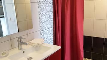 Un baño con lavamanos blanco, mueble rojo y cortina de ducha.
