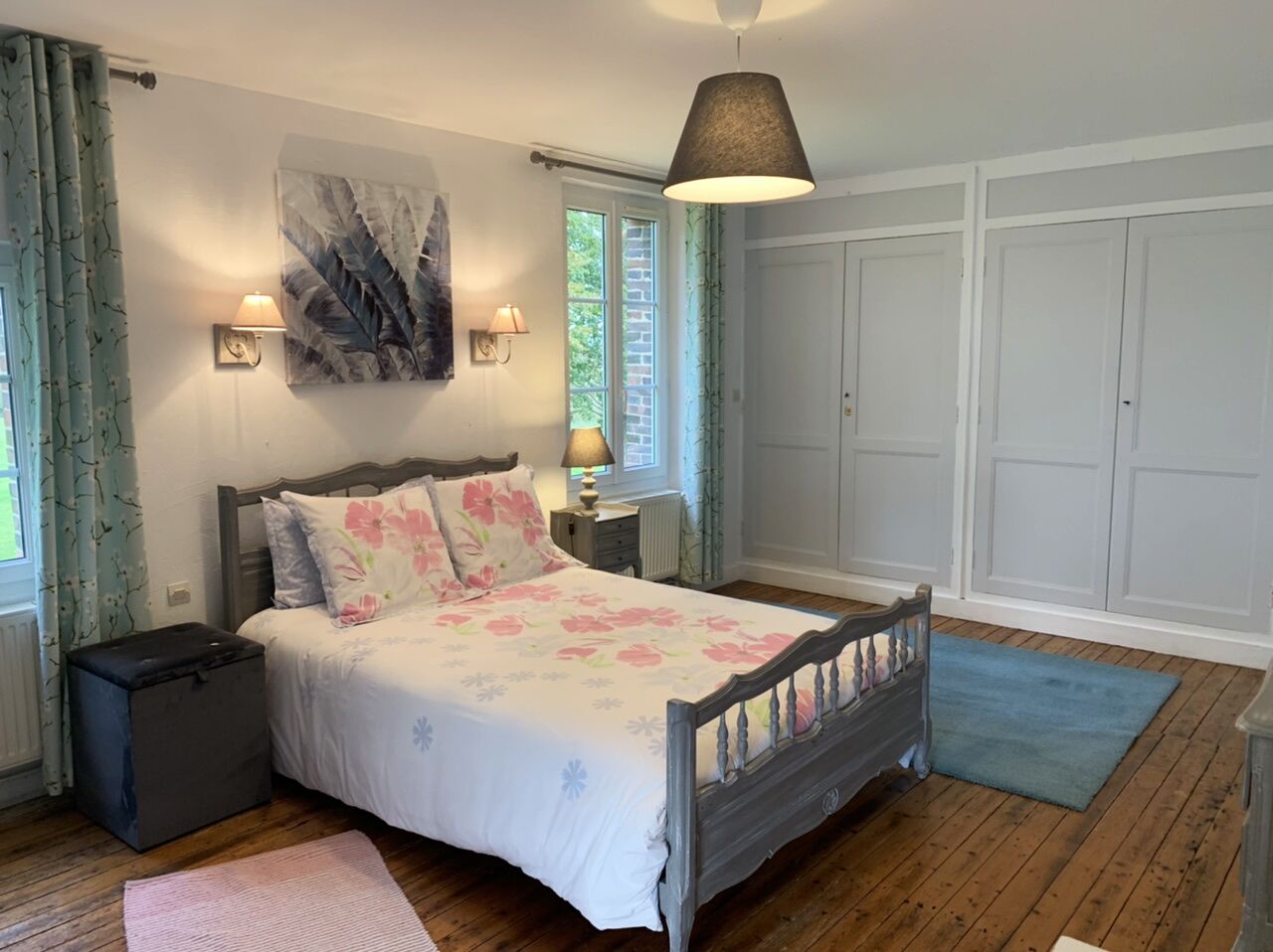 A bedroom with a wooden bed, floral bedding, a nightstand, a lamp, a radiator, and a wardrobe.