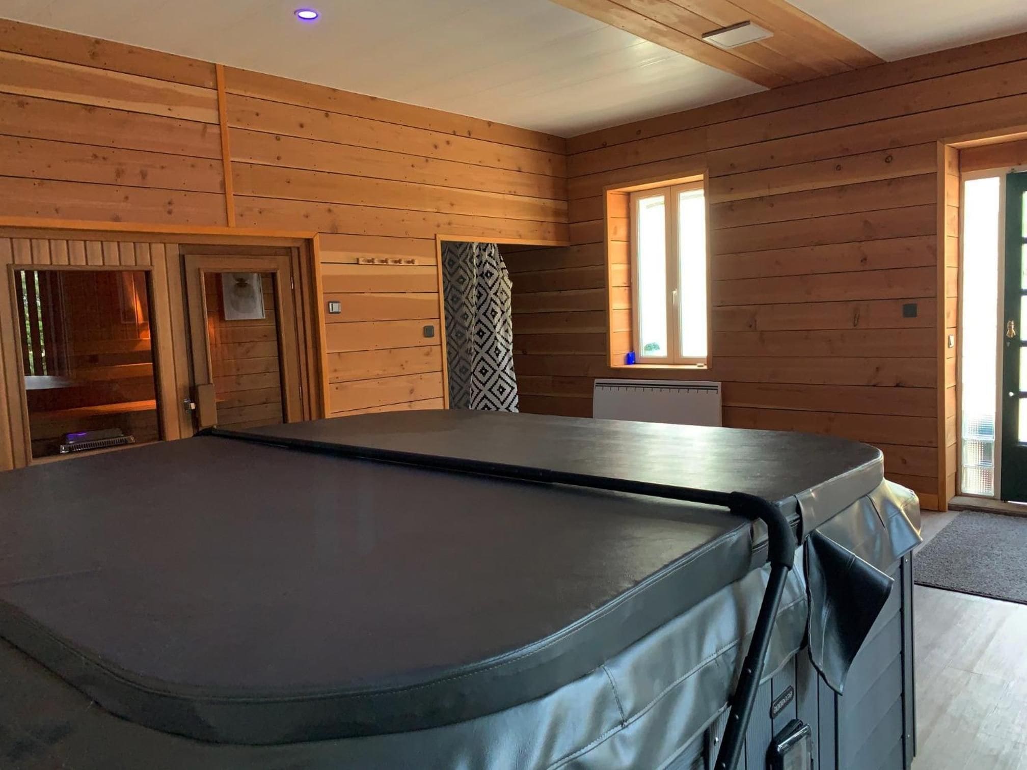 A room with wooden walls, a massage table, a window, and a door.