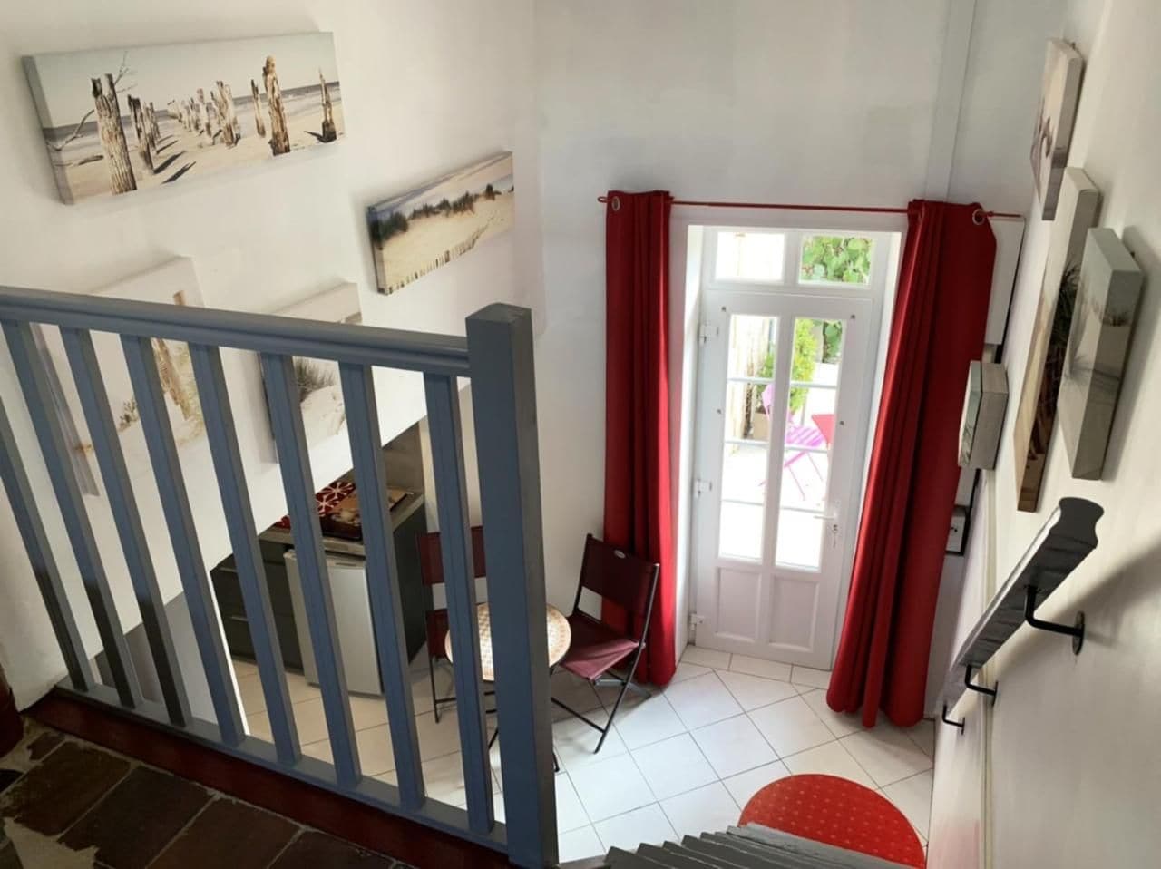 A room with a staircase, a dining area with chairs, a door with red curtains, and a wall with artwork.