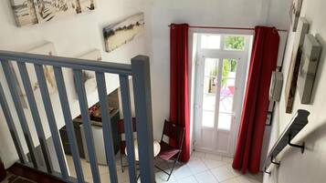 A room with a staircase, a dining area with chairs, a door with red curtains, and a wall with artwork.