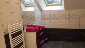 A bathroom with a skylight, a white towel rack, a vanity with a mirror, and a black tiled wall.