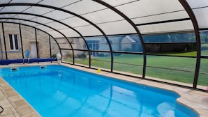 A swimming pool with a glass enclosure, stone tiles, and a view of a grassy yard. - La Part des Anges (Rubercy)