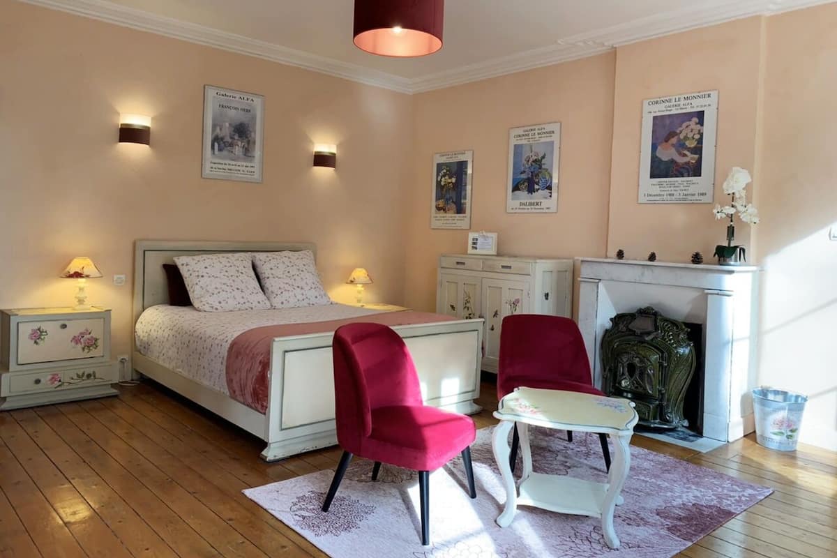 Un dormitorio con una cama, dos sillas rojas, una mesa blanca, una chimenea y luces en la pared.