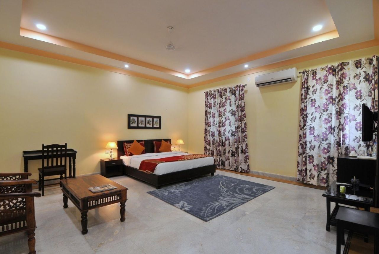 A hotel room with a bed, a desk, a chair, a TV, and an air conditioning unit.