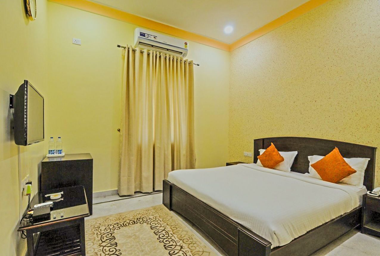 A hotel room with a bed, a TV, a minibar, and an air conditioning unit.