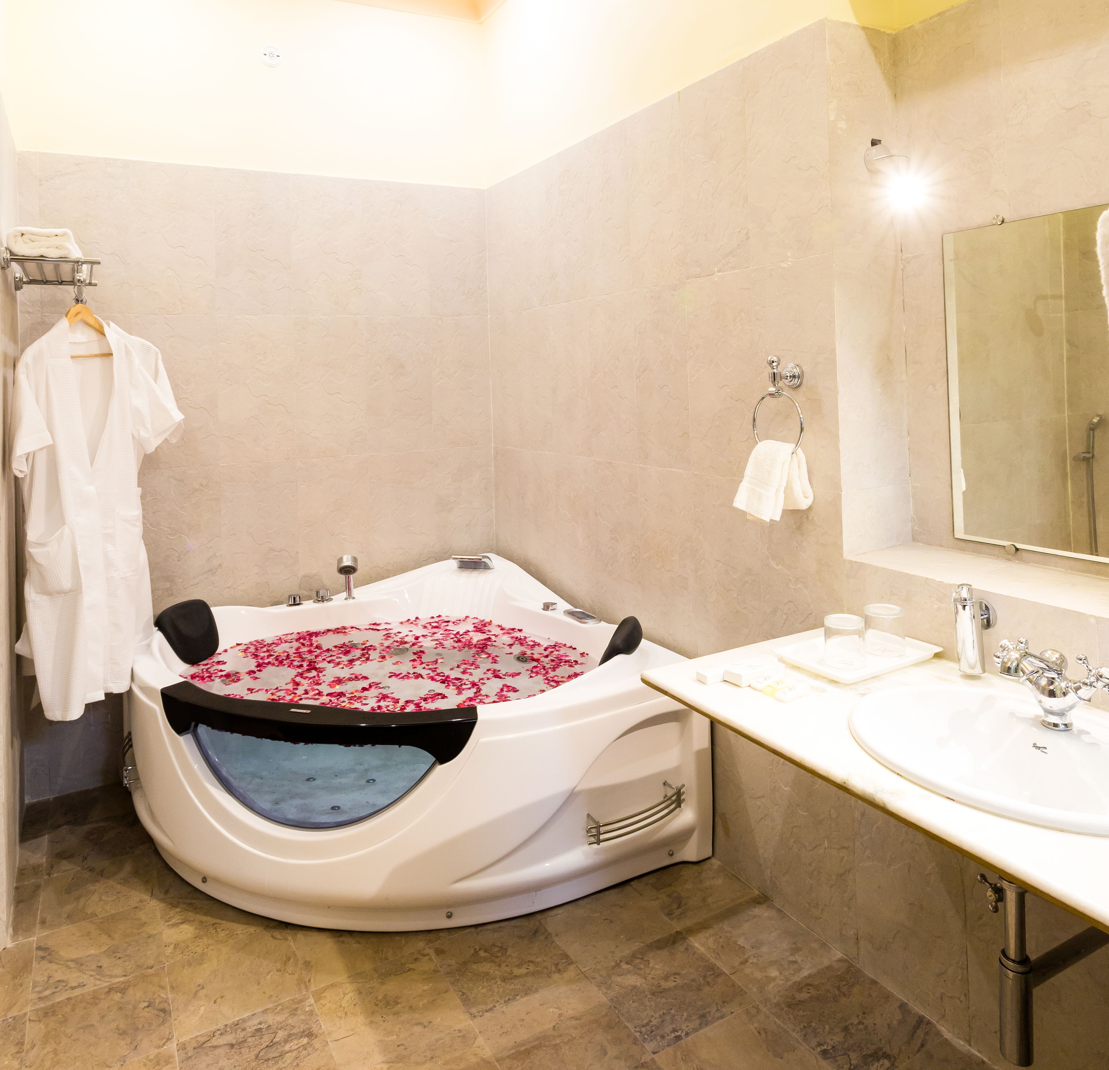 A bathroom with a large bathtub filled with rose petals, a sink, and a mirror.