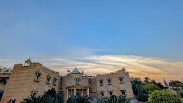 A historic building with a central dome and multiple arches, surrounded by well-maintained gardens and a clear sky.