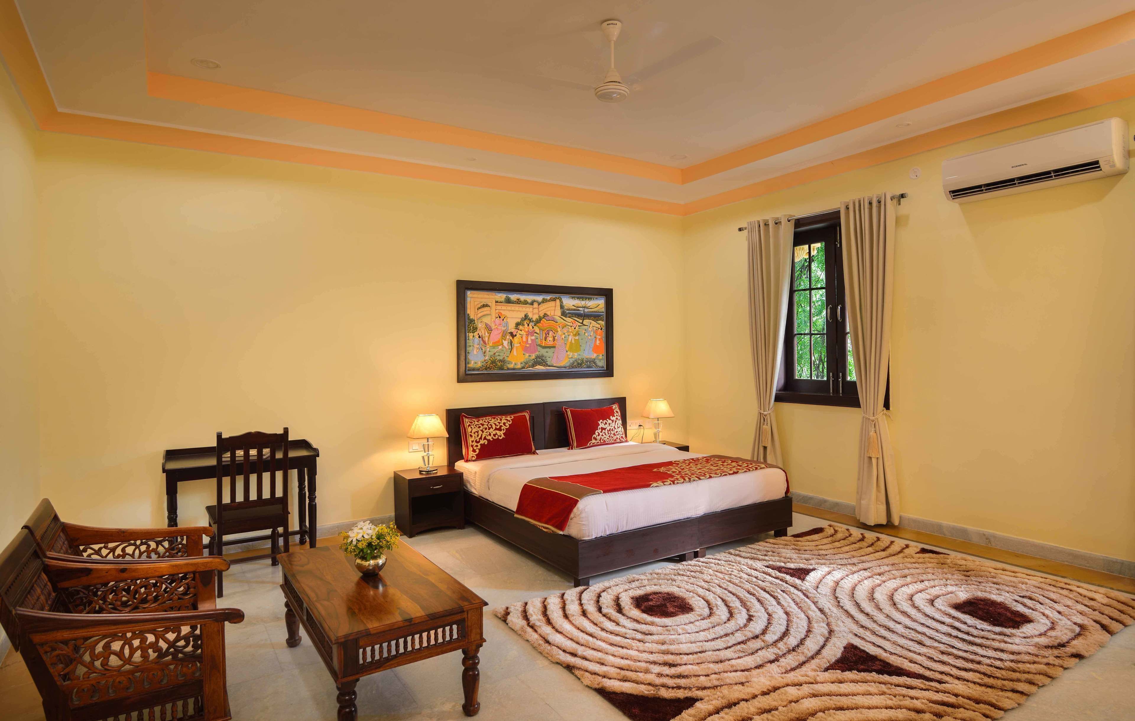 A bedroom with a bed, two nightstands, a wooden table, a chair, a decorative rug, and a painting on the wall.