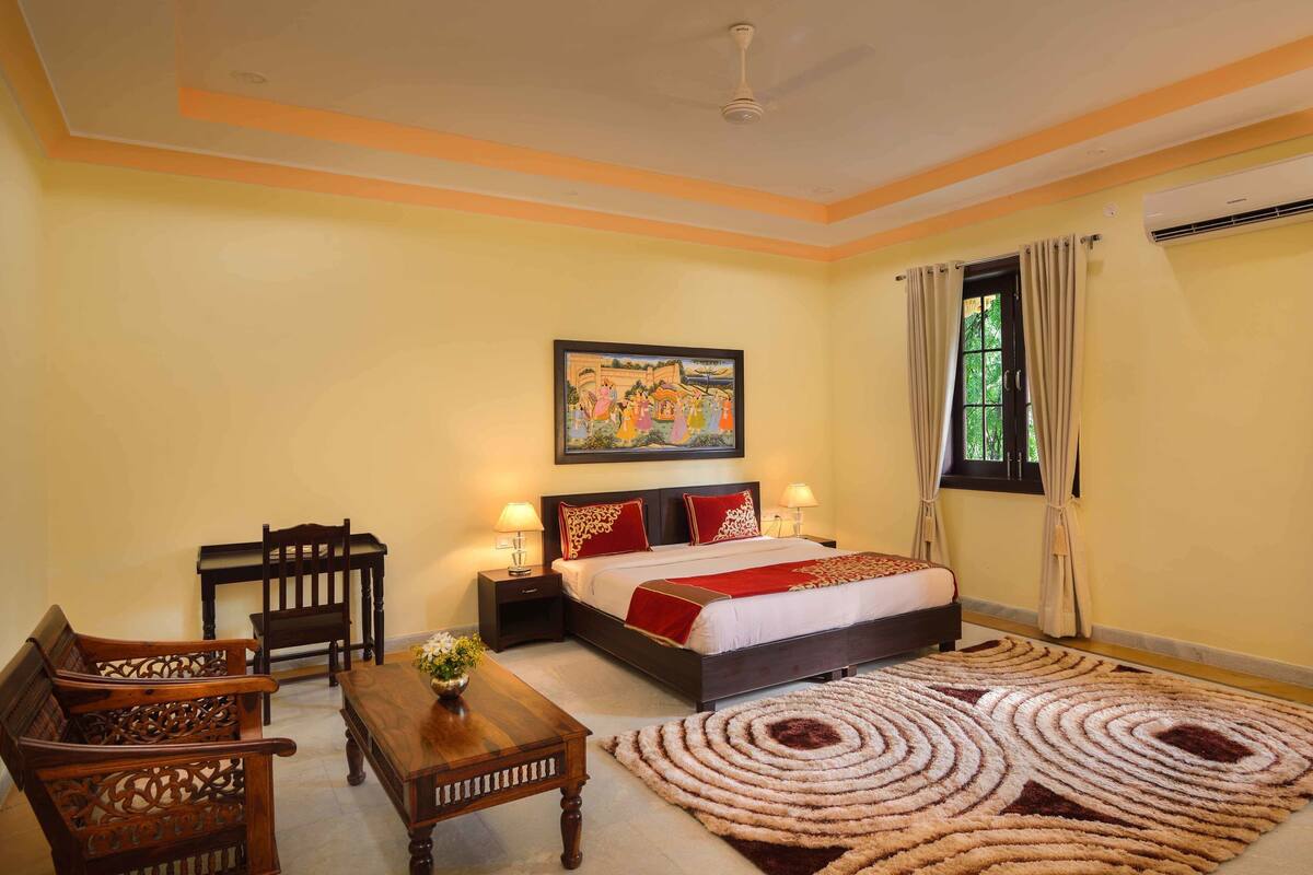 A bedroom with a bed, two nightstands, a wooden table, a chair, a decorative rug, and a painting on the wall.
