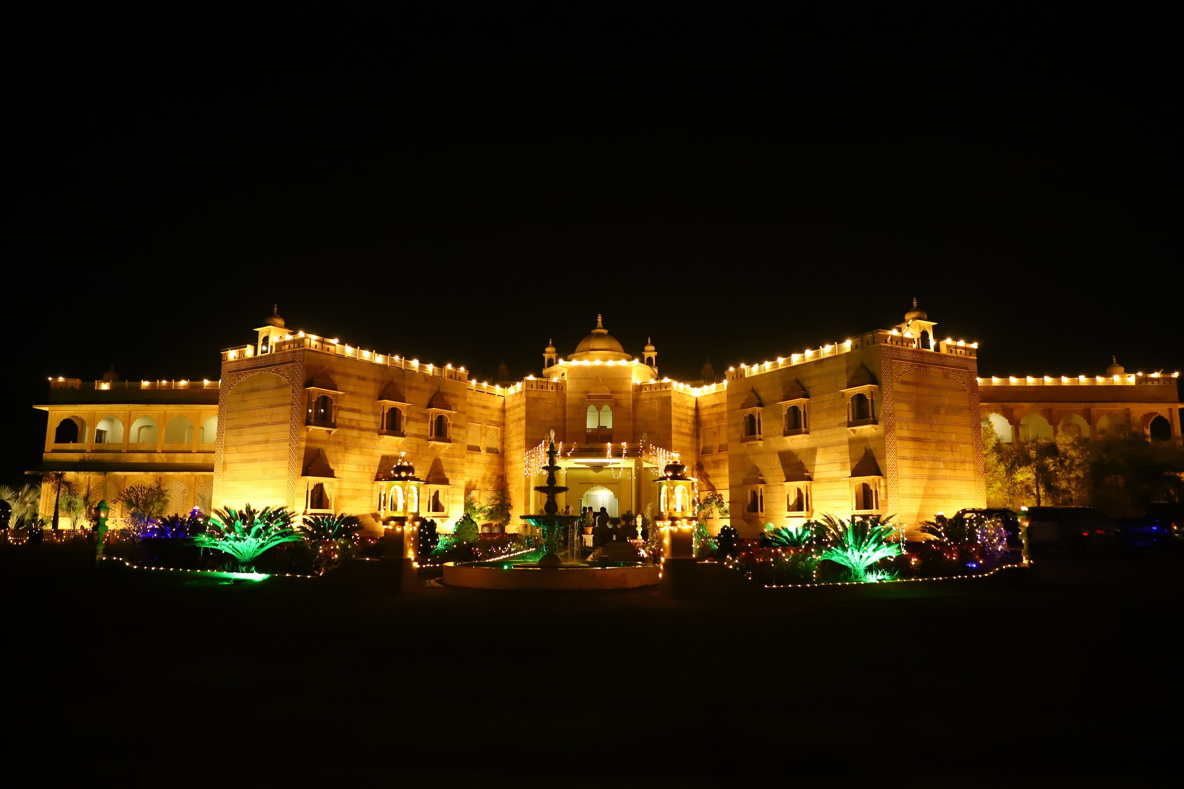 A large, illuminated building with multiple towers and domes, surrounded by well-lit gardens and pathways.