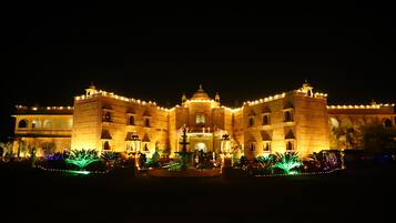 A large, illuminated building with multiple towers and domes, surrounded by well-lit gardens and pathways.