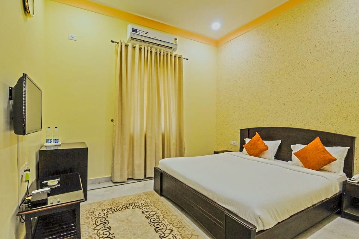 A hotel room with a bed, a TV, a minibar, and an air conditioning unit.