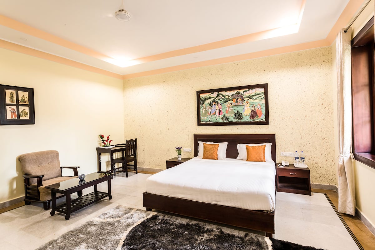 A bedroom with a large bed, a chair, a small table, and a painting on the wall.