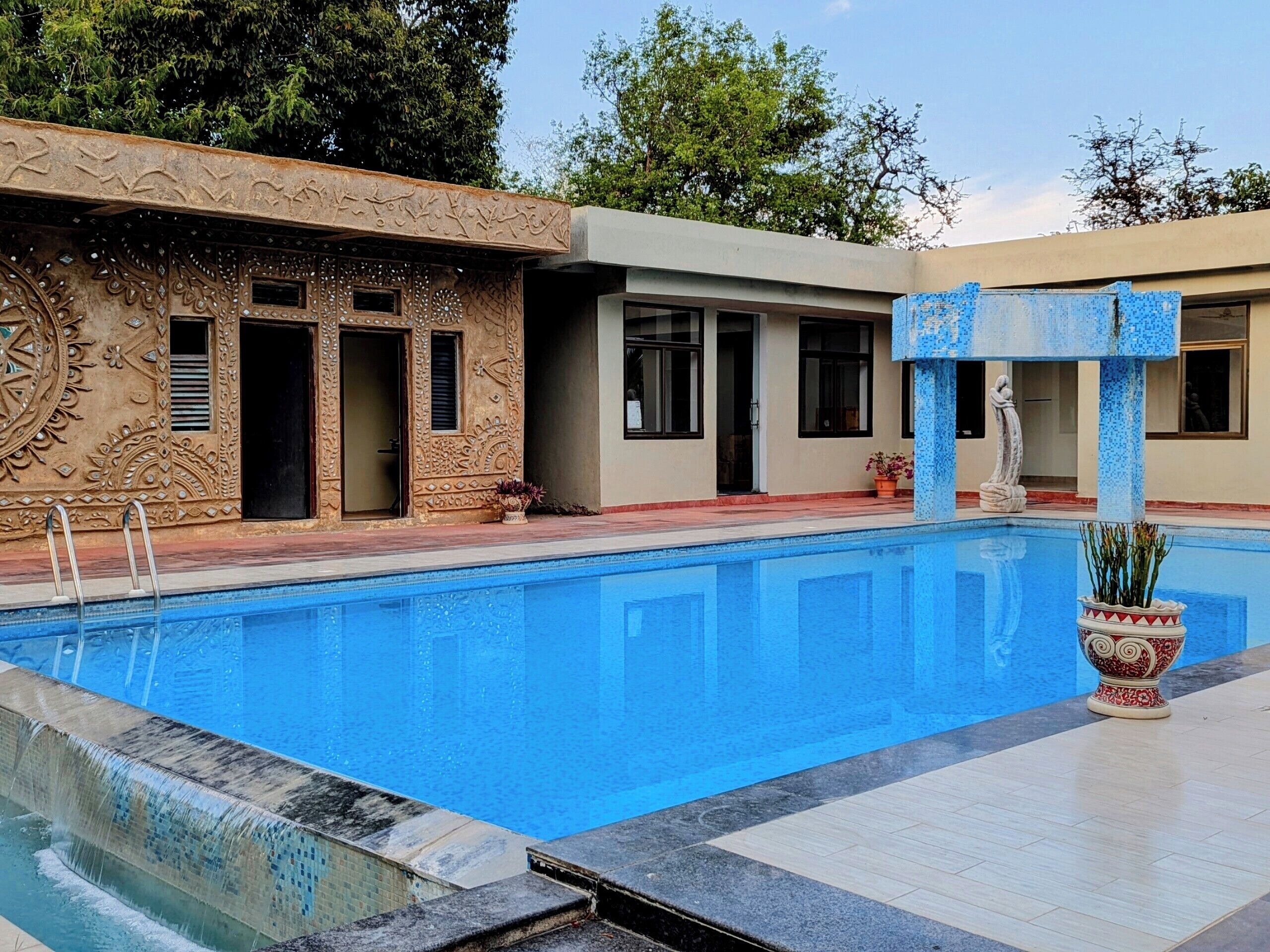 A swimming pool with a decorative fountain, a building with intricate carvings, and a statue.