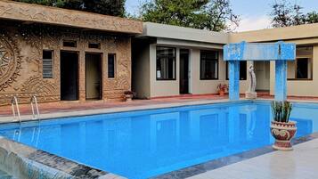 A swimming pool with a decorative fountain, a building with intricate carvings, and a statue.
