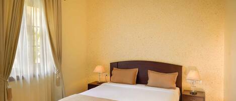A hotel room with a bed, two bedside lamps, a ceiling fan, and an air conditioning unit.