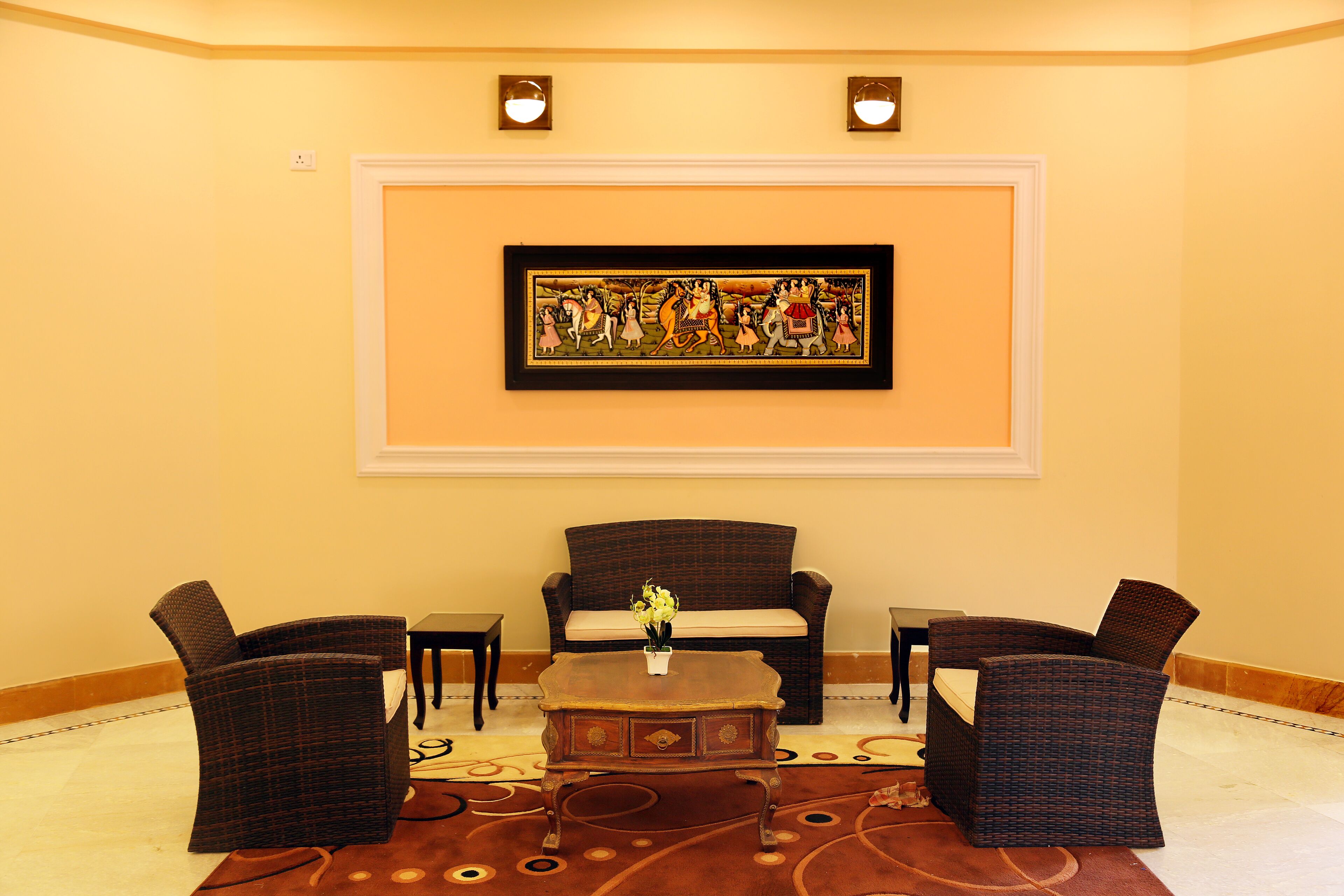 A lobby with a brown wicker sofa, two armchairs, a small table with a vase, and a framed picture on the wall.