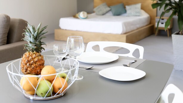 A neatly arranged breakfast table with a fruit bowl, plates, and cutlery. A bed with a wooden headboard and pillows is visible in the background. - Cap Heureux Villas (Cap Malheureux)