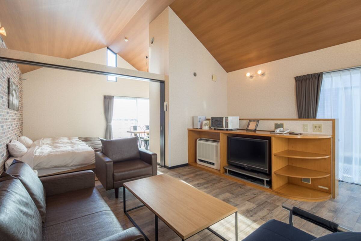 Un espacio habitable moderno y de concepto abierto con un sofá, una mesita, un televisor y una cocina equipada con microondas y cafetera.