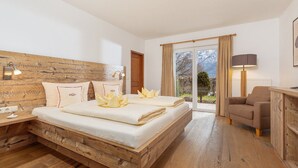 A bedroom with a wooden headboard, a bed with white bedding, a desk with a chair, and a view of the outdoors.