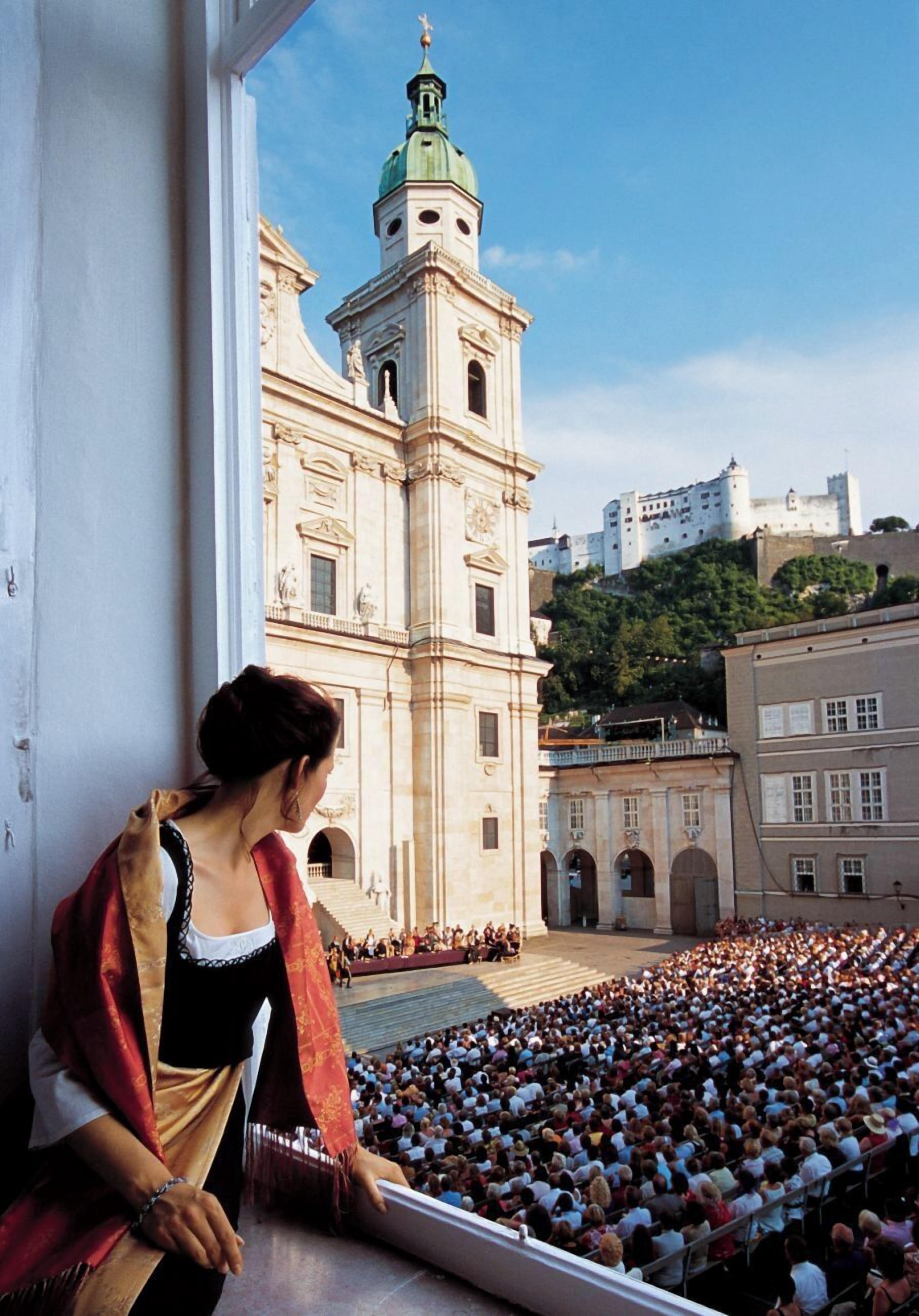 A large crowd gathered in an open square with a historic building in the background.