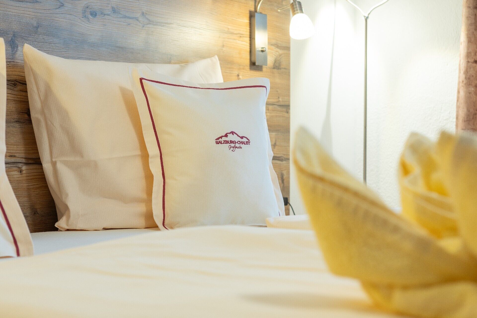 Una camera d'albergo con una testiera in legno, biancheria da letto bianca e un cuscino con il logo 'Salzburg-Chalet'.