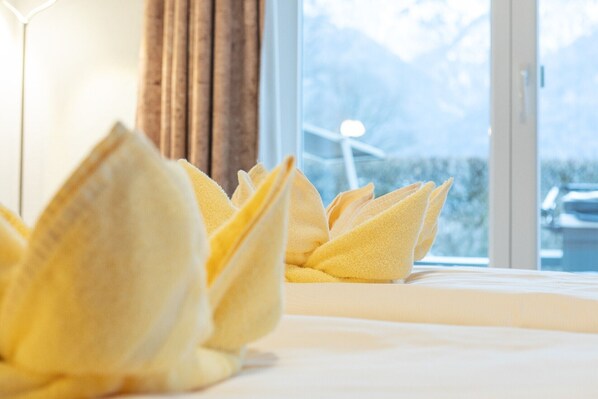 Habitación de hotel con toallas ordenadamente dobladas en la cama y vistas a montañas y una turbina eólica a través de la ventana.