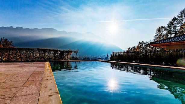 A clear swimming pool with a wooden deck and a view of mountains in the background.