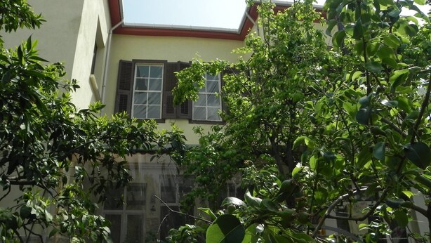 A building with a sloped roof, a window with shutters, and dense foliage in front. - Lotus Garden Hostel (Izmir)