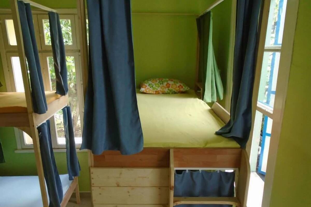 A bunk bed room with a wooden frame, a single bed with a floral pillow, and a window with curtains.